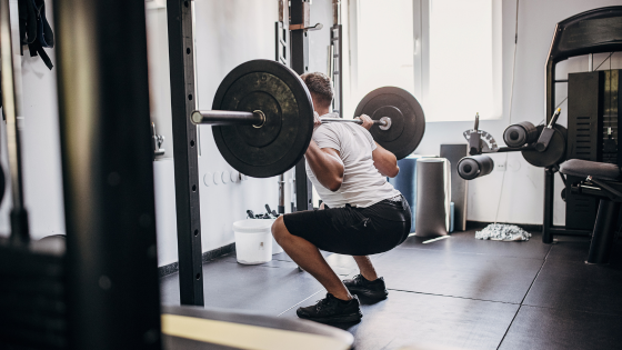 A man does weighted squats in a gym after taking a high-stim pre-workout
